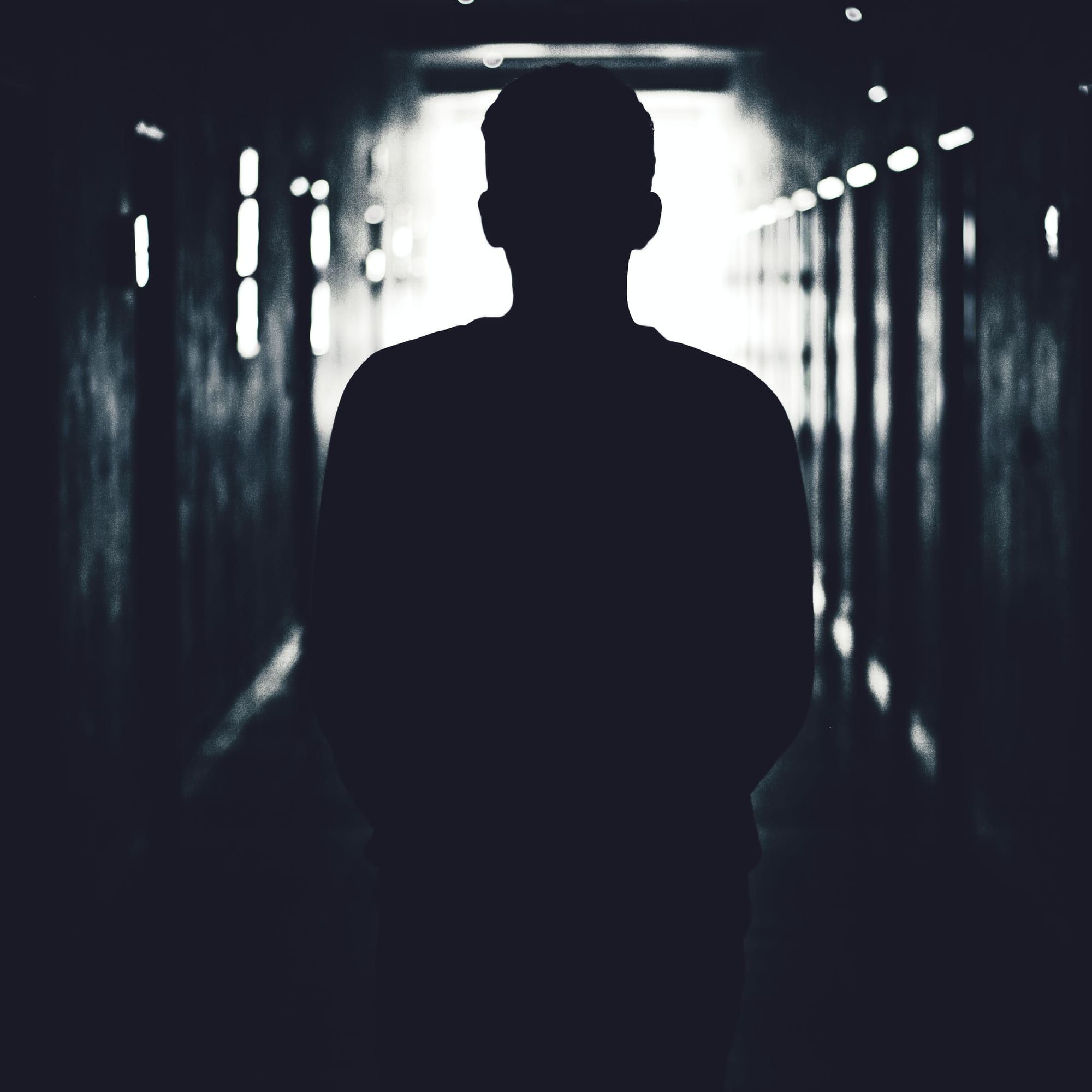 Silhouette eines Mannes in einem dunklen Gang vor gleißendem Licht